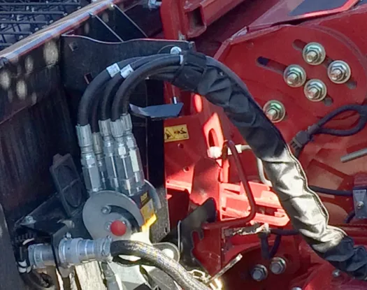 Hydraulic hoses bundled in a black sleeve on red farm equipment