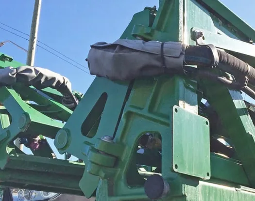 Grey sleeve protecting hoses on a green farm implement