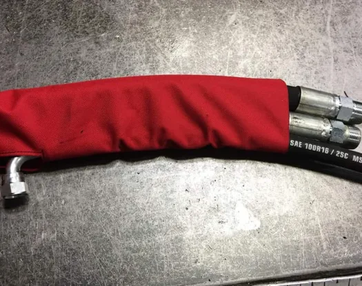 Red sleeve on a hydraulic hose, with a fitting coming out through an access opening